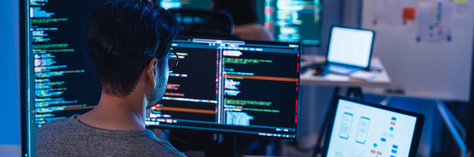 An individual working with several screens of multicolored computer code