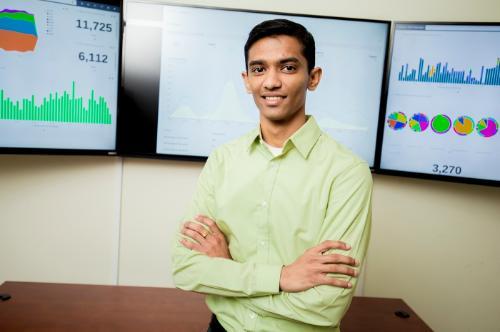 A student leaning against a desk in front of wall-mounted monitors