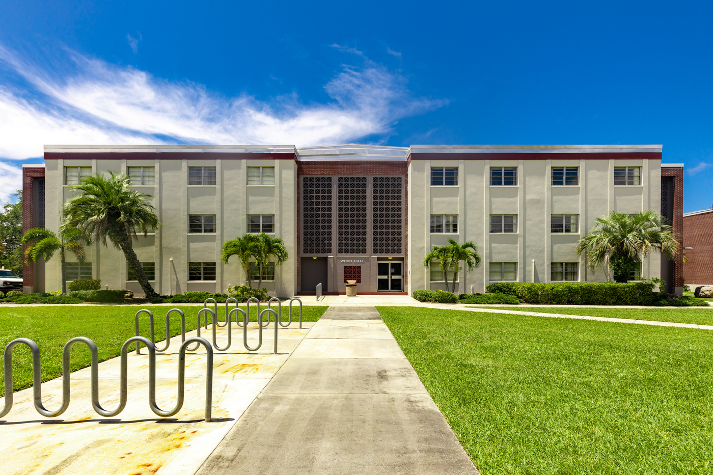 Wood hall, a three story stucco and brick facade building surrounded by palm trees, walkways and green lawn on a sunny day