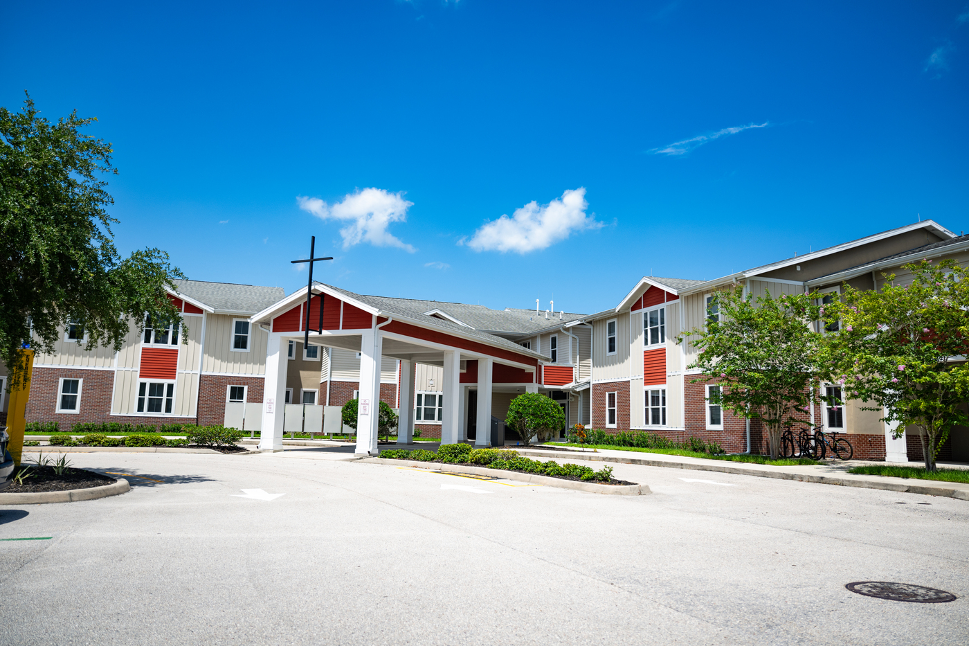 Entrance to Mary Star of the Sea Newman Hall on a bright sunny day. A covered entryway sits in the centre of the building with a cross on top.